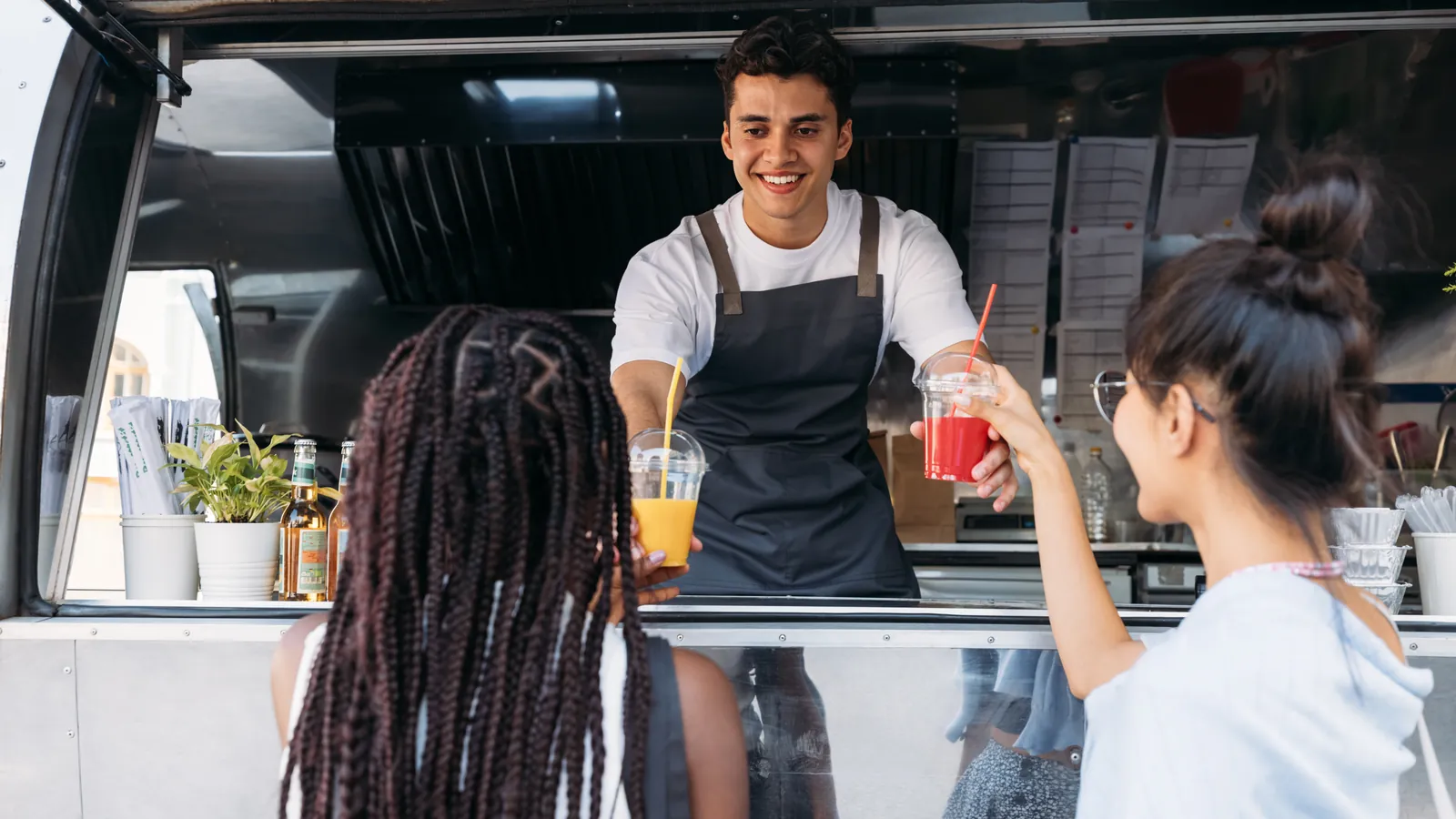 Junger Imbissbetreiber bedient Kundinnen am Foodtruck