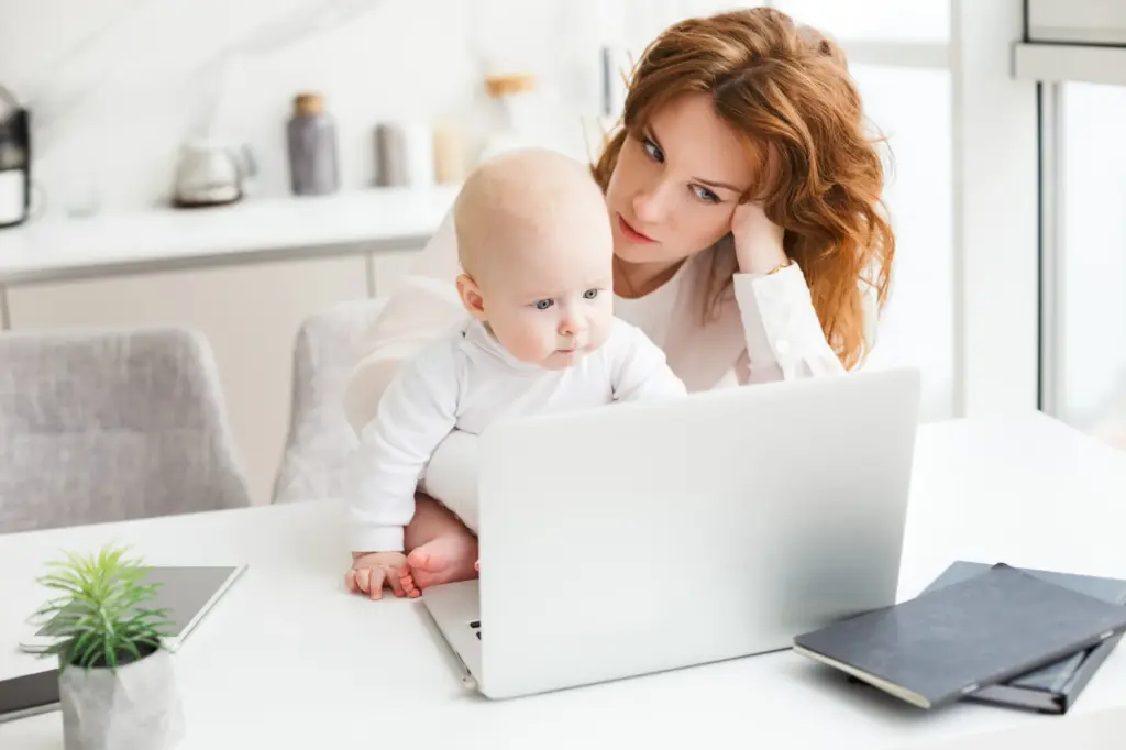Mutter mit Baby arbeitet zu Hause am Laptop